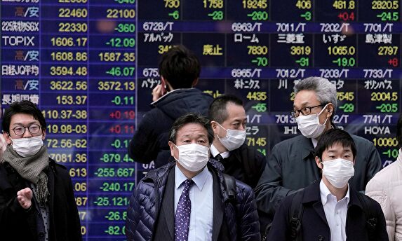 Varios viandantes pasan frente a una pantalla con información bursátil, este miércoles, en Tokio. | EFE