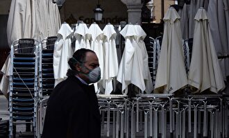 Un hombre ataviado con una mascarilla pasa por delante de una terraza recogida de un bar. | EFE