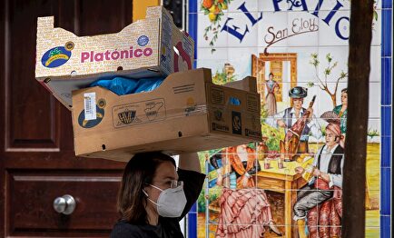 Una mujer con mascarilla porta dos cajas sobre su cabeza en el barrio de Triana de Sevilla | EFE