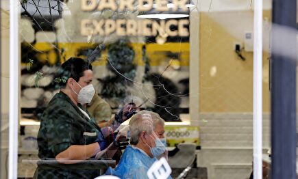 Una peluquera corta el pelo a un cliente protegidos ambos con mascarillas y guantes este sábado, en Valencia. | EFE