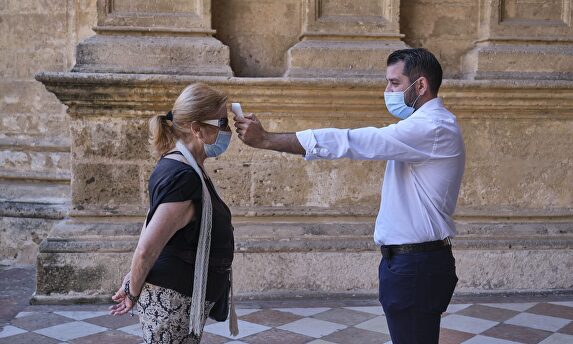 Un operario toma la temperatura de la persona a la entrada de la catedral de Málaga. | Cordon Press