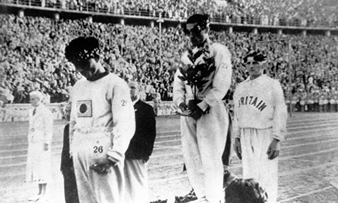 Sohn recibe la medalla de oro con la mirada al suelo y tapándose la bandera de Japón. | Archivo