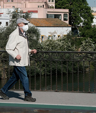 Una hombre mayor protegido con mascarilla pasea por el puente de Triana I Europa Press