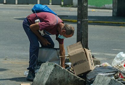 Un hombre buscando comida en la basura en Venezuela | Alamy
