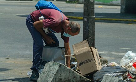 Un hombre buscando comida en la basura en Venezuela | Alamy