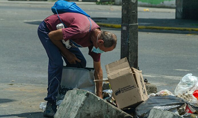 Un hombre buscando comida en la basura en Venezuela | Alamy