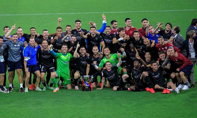 Los jugadores del Huesca posan con el trofeo de campeones de LaLiga SmartBank sobre el césped de El Molinón. | EFE