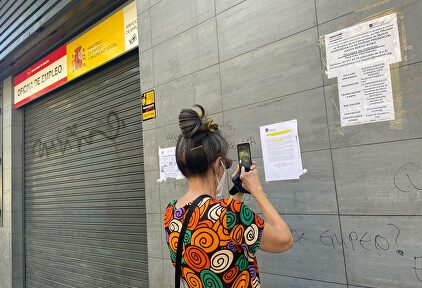 Una mujer fotografía uno de los carteles colocados en la fachada de una oficina del SEPE I Europa Press