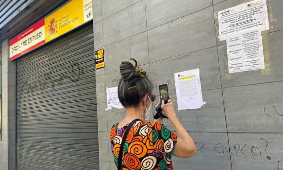 Una mujer fotografía uno de los carteles colocados en la fachada de una oficina del SEPE I Europa Press