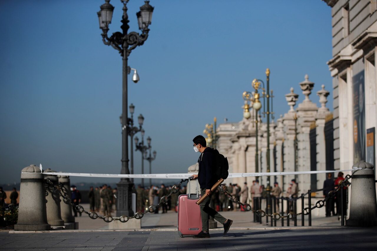 Un joven con su maleta pasa ante el Palacio Real de Madrid | EFE