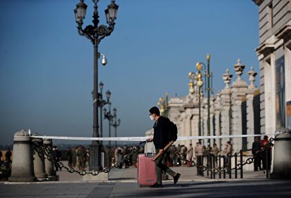 Un joven con su maleta pasa ante el Palacio Real de Madrid | EFE